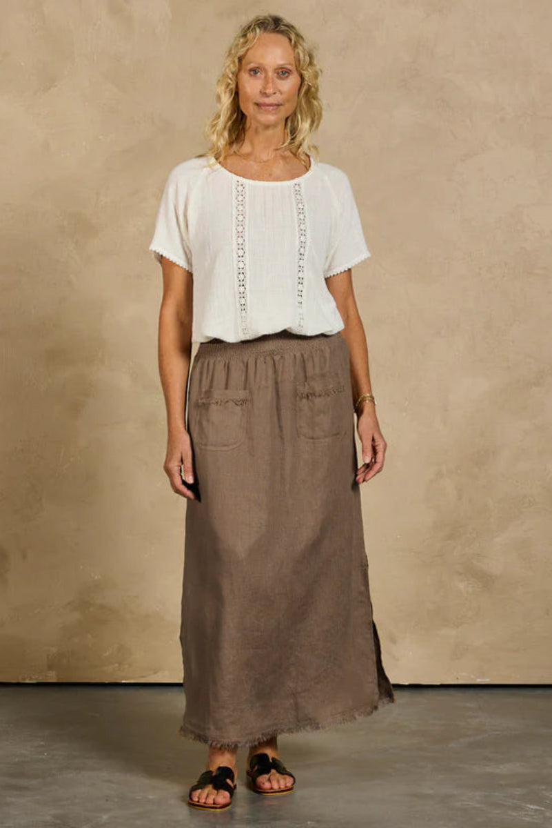 Woman wearing a white top and brown skirt against a beige wall.