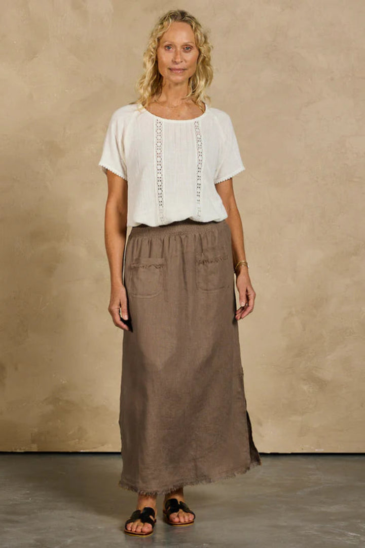 Woman wearing a white top and brown skirt against a beige wall.