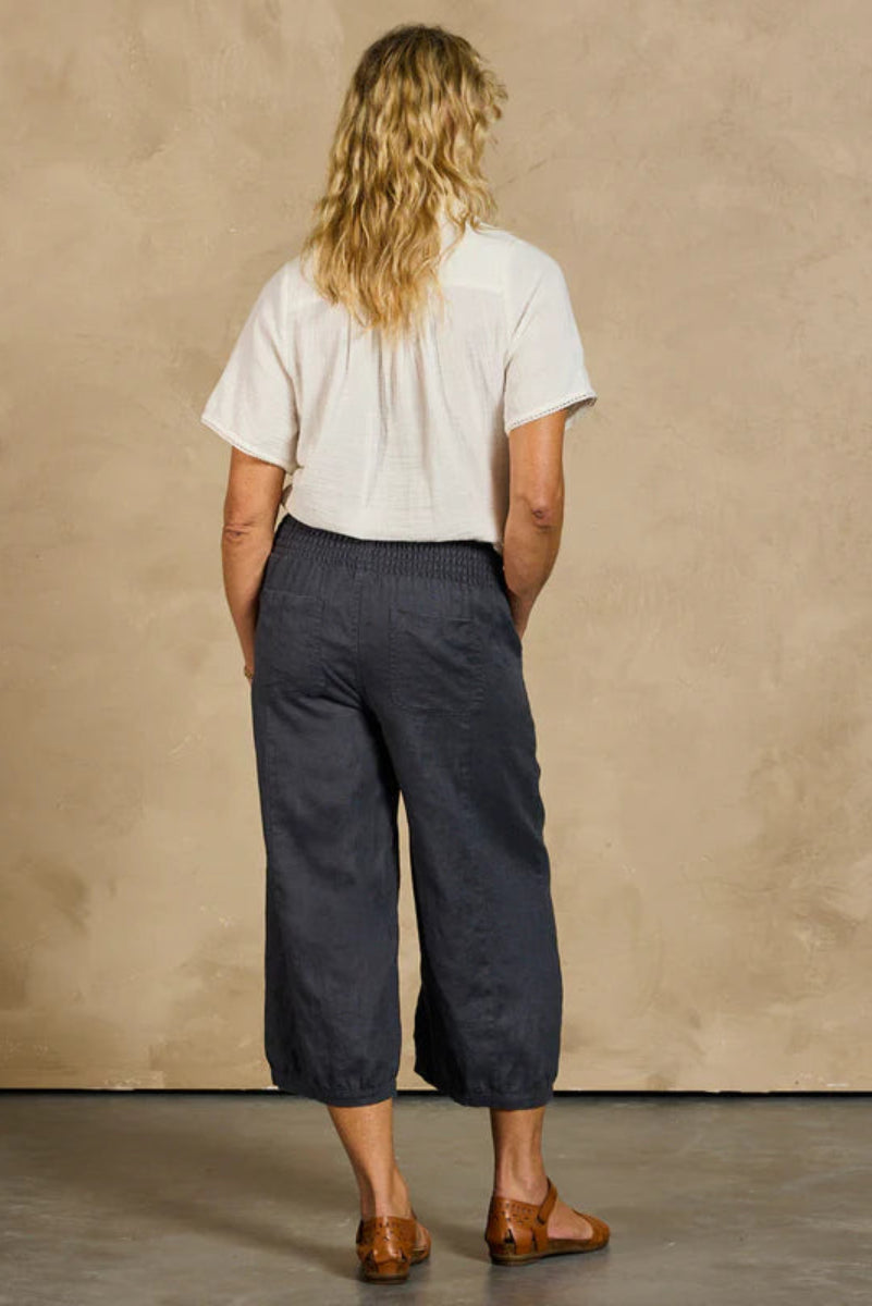 Person wearing a white shirt and dark pants against a beige wall