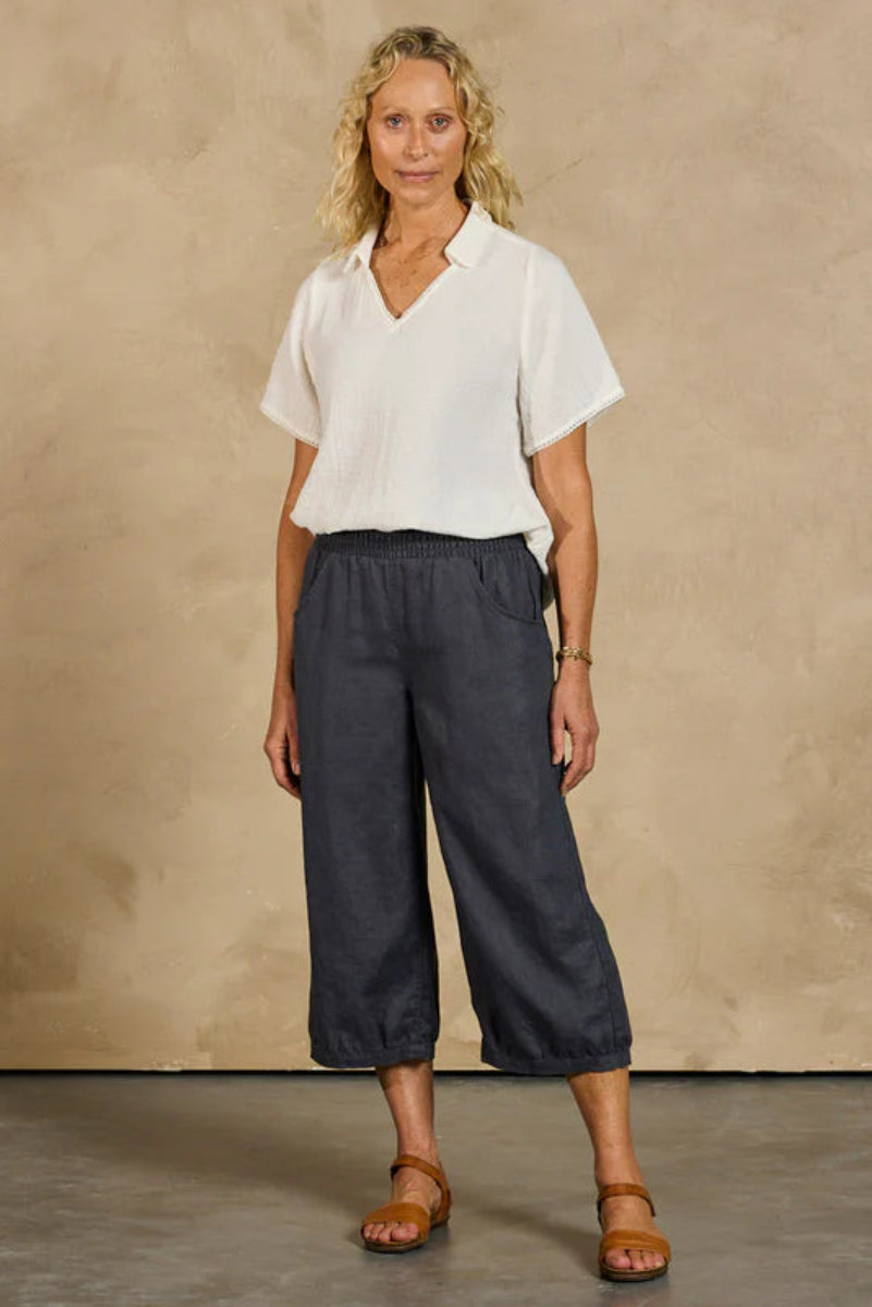 Woman wearing a white blouse and dark pants against a beige background