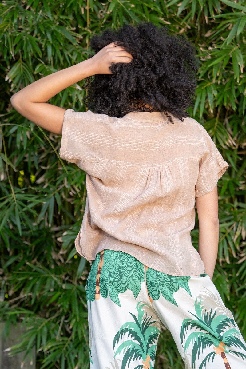 Person wearing a beige top and green palm tree pants standing against a leafy background