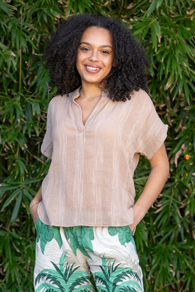 Woman wearing a beige blouse and tropical print pants standing against a green leafy background