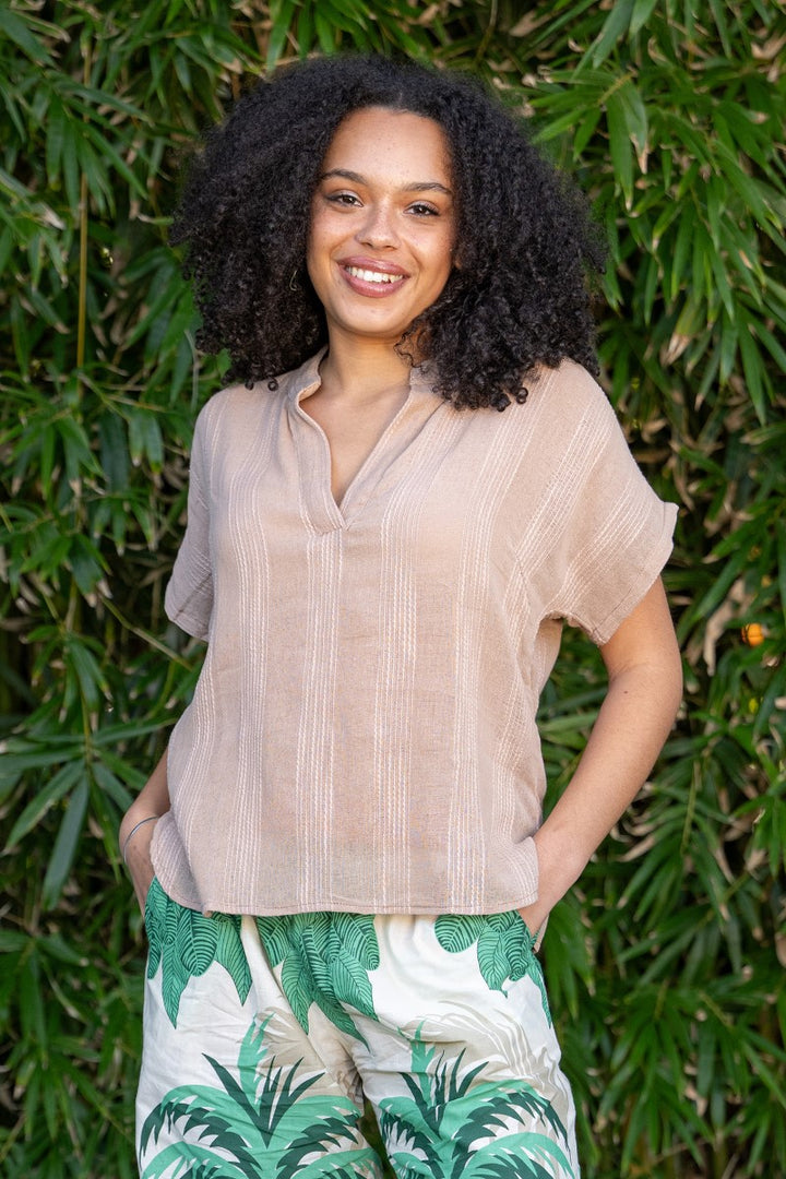 Woman wearing a beige blouse and tropical print pants standing against a green leafy background