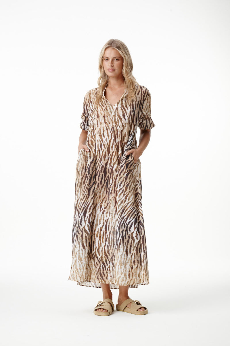 A woman modeling a long-sleeved maxi dress with a brown and beige animal print pattern, standing against a plain white studio background.