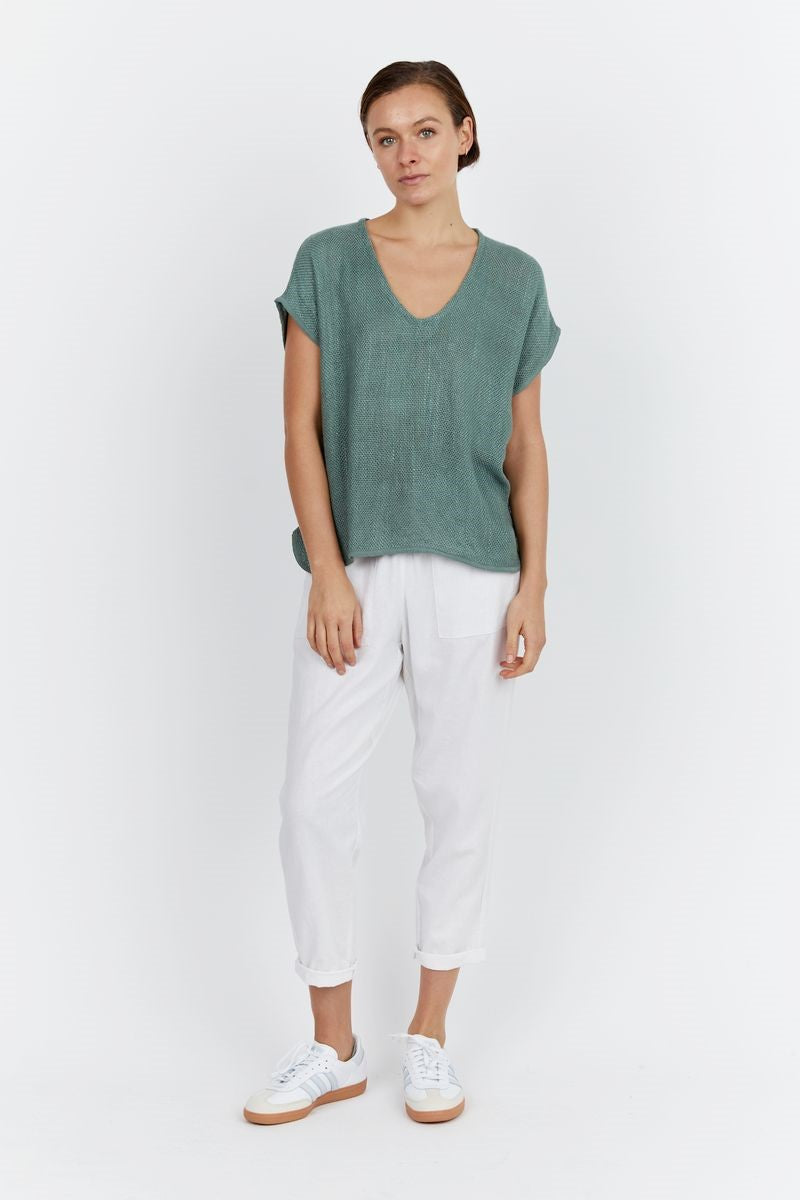 Woman wearing a green top and white pants on a white background