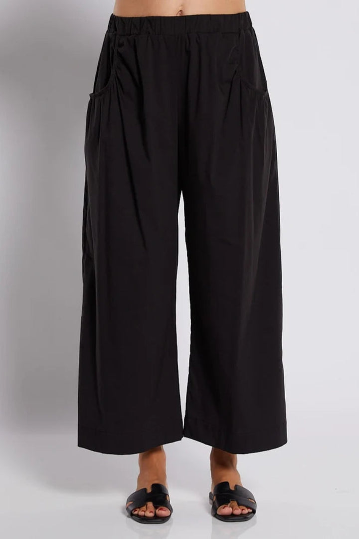 Black wide-leg cropped pants with an elastic waistband and side pockets, shown on a model wearing black slide sandals against a light gray studio background.