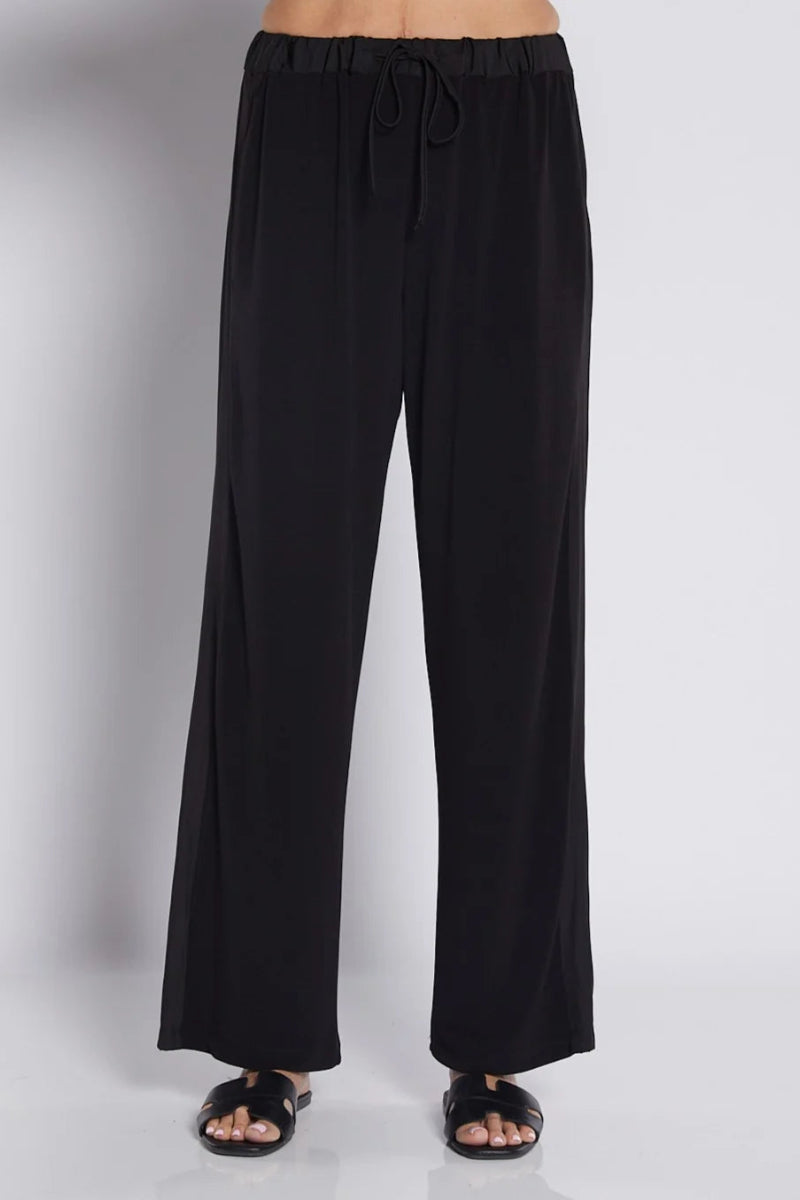 Black wide-leg drawstring pants shown on a model from the waist down, paired with black slide sandals against a light gray studio background.