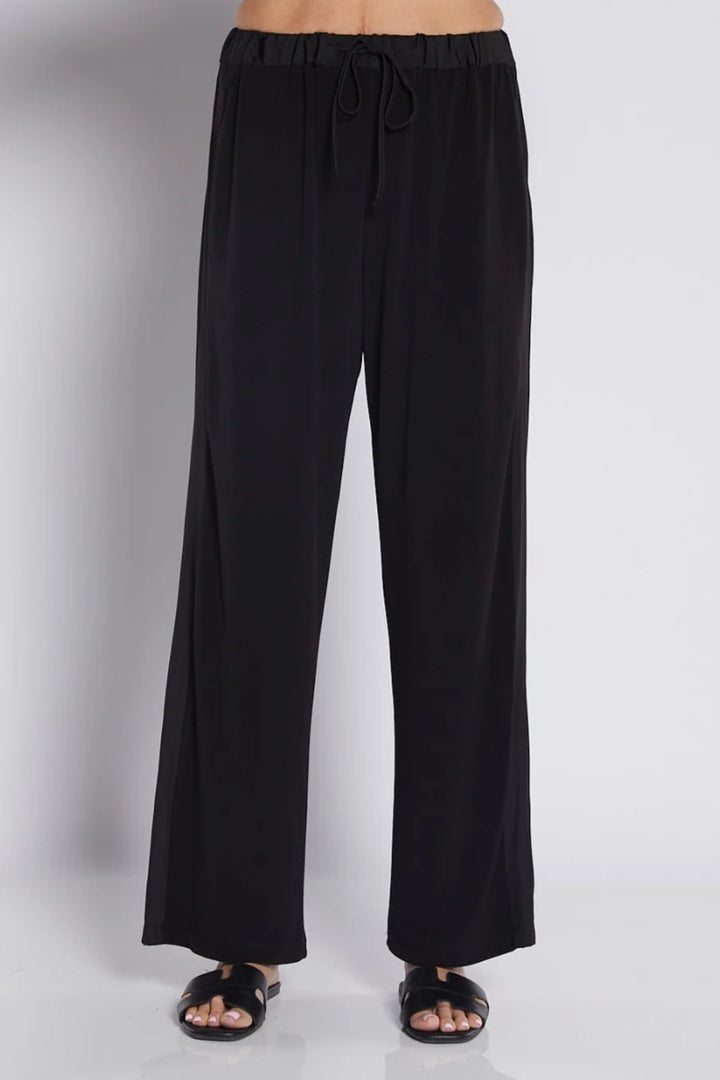 Black wide-leg drawstring pants shown on a model from the waist down, paired with black slide sandals against a light gray studio background.
