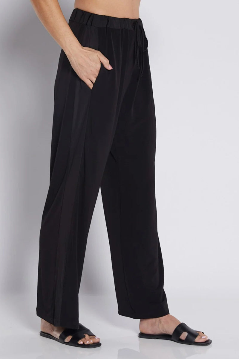 Black wide-leg trousers with an elastic waistband and side pockets, shown on a model wearing black slide sandals against a light gray studio background.