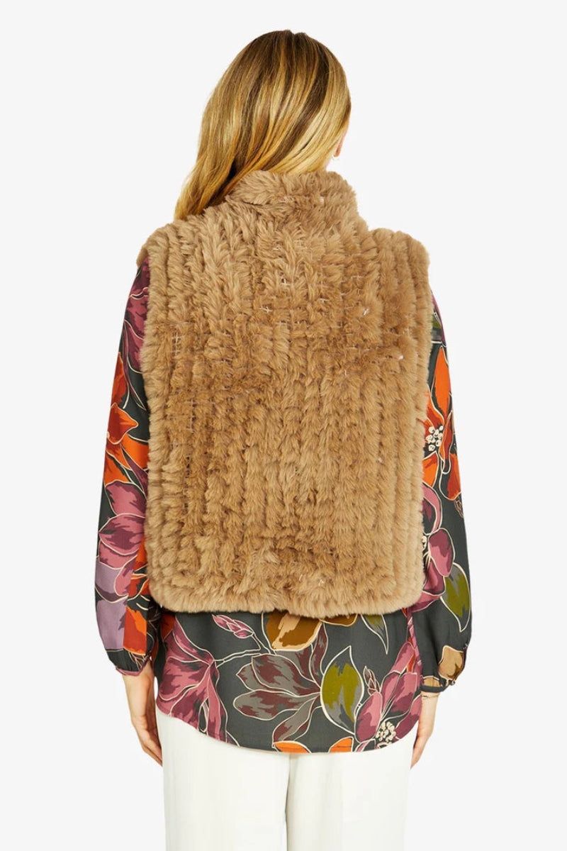 Woman wearing a brown fur vest over a colorful floral blouse on a white background