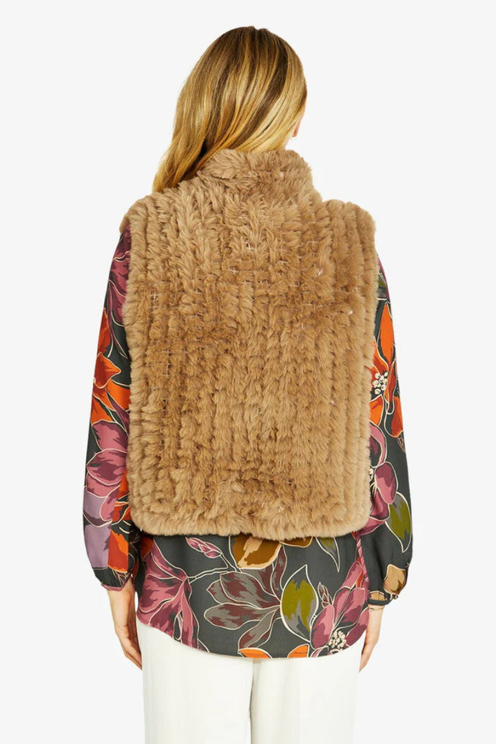 Woman wearing a brown fur vest over a colorful floral blouse on a white background