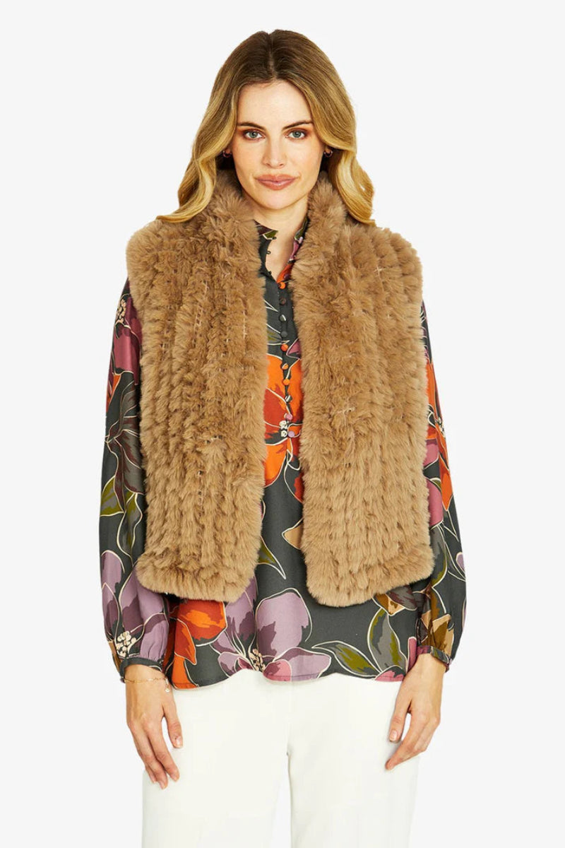 Woman wearing a brown fur vest over a colorful floral blouse on a white background