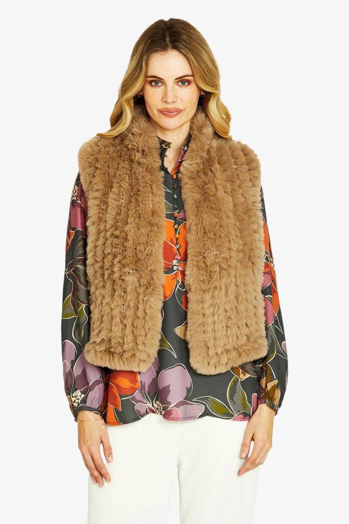 Woman wearing a brown fur vest over a colorful floral blouse on a white background