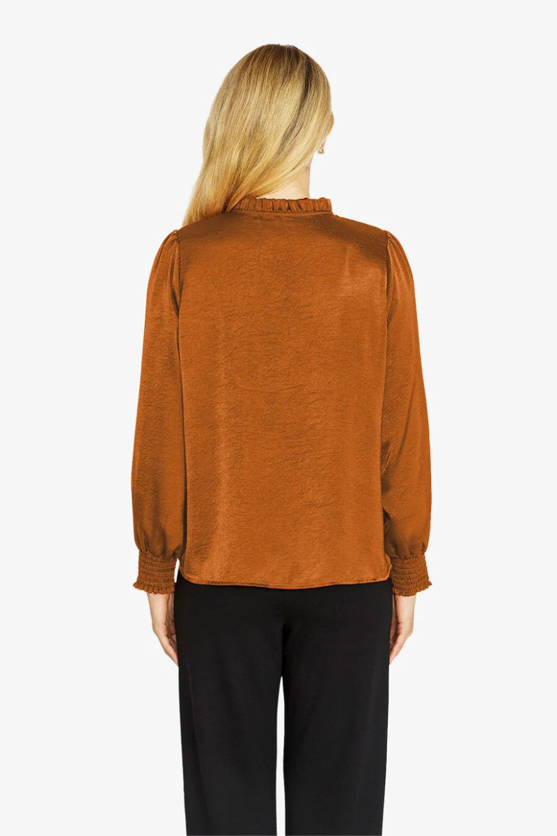 Person wearing a rust-colored blouse with long sleeves on a white background