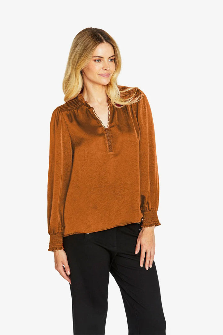 Woman wearing a rust-colored blouse and black pants on a white background