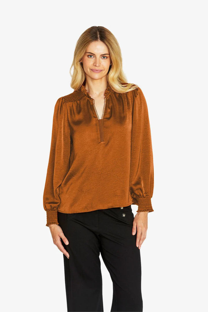 Woman wearing a rust-colored blouse with long sleeves on a white background