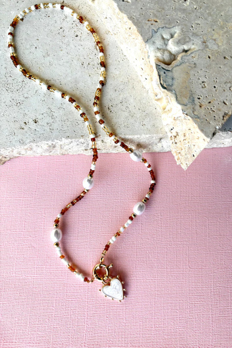 Necklace with heart charm on a pink and gray textured background