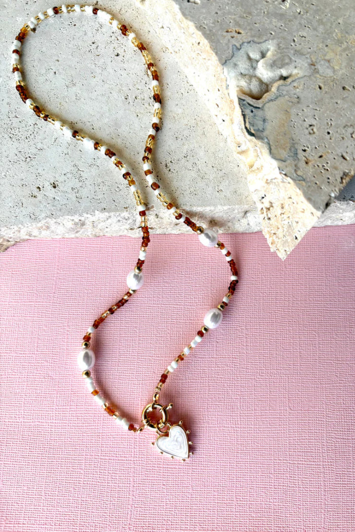 Necklace with heart charm on a pink and gray textured background