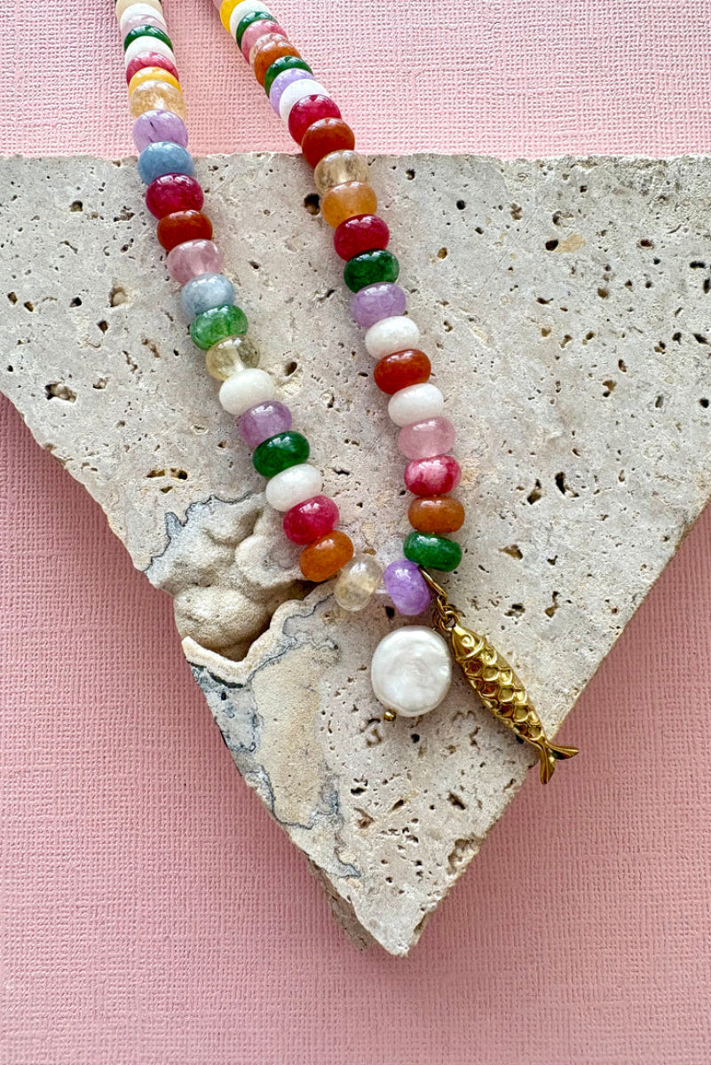 Colorful beaded necklace with a gold clasp on a textured stone surface with a pink background