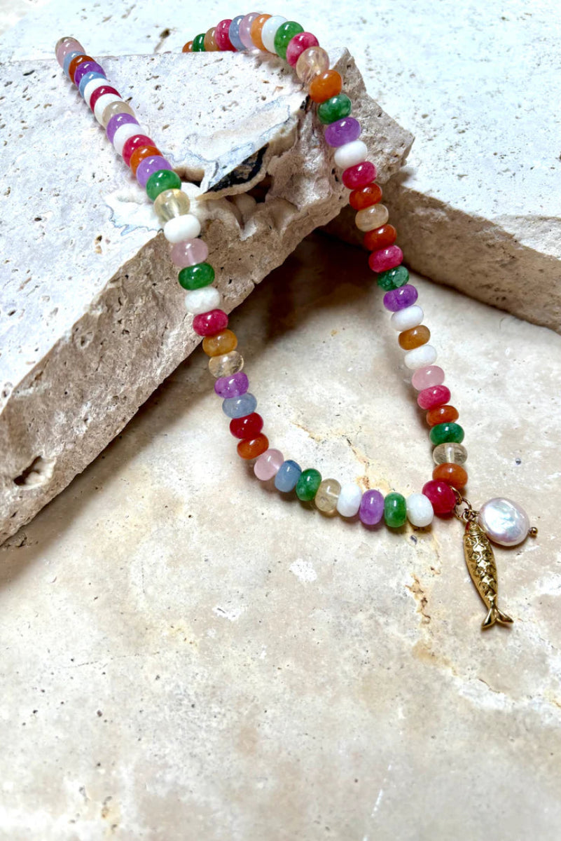 Colorful beaded bracelet with a fish charm on a textured surface