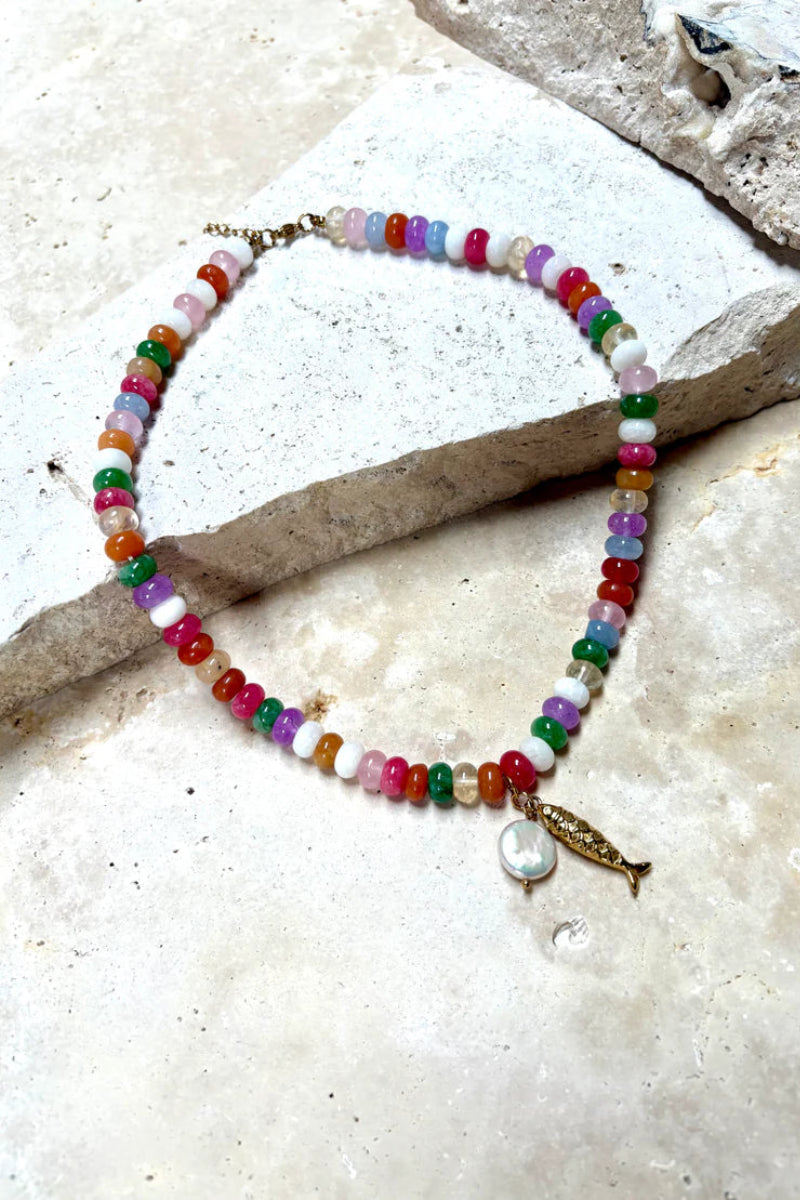 Multicolored beaded bracelet with a gold charm on a textured stone surface