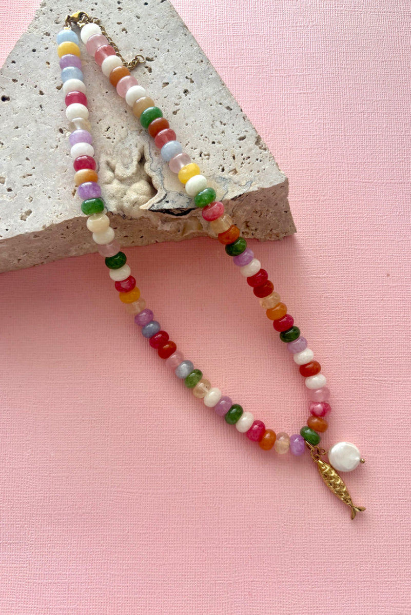 Colorful beaded necklace on a pink surface with a concrete block background