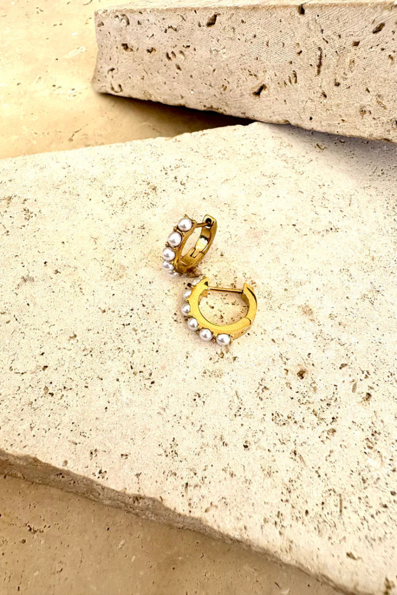 Gold and pearl earring on a textured stone surface