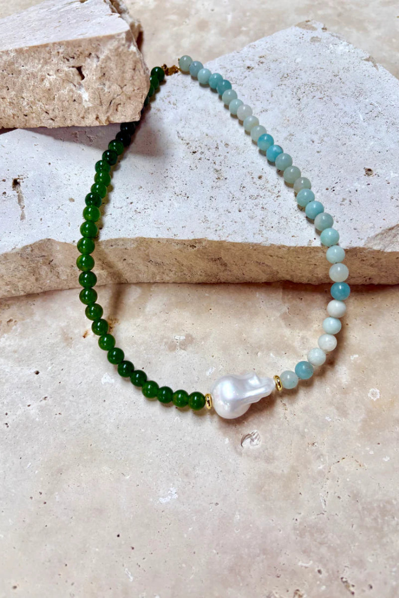 Beaded bracelet with green and blue beads and a pearl on a stone surface