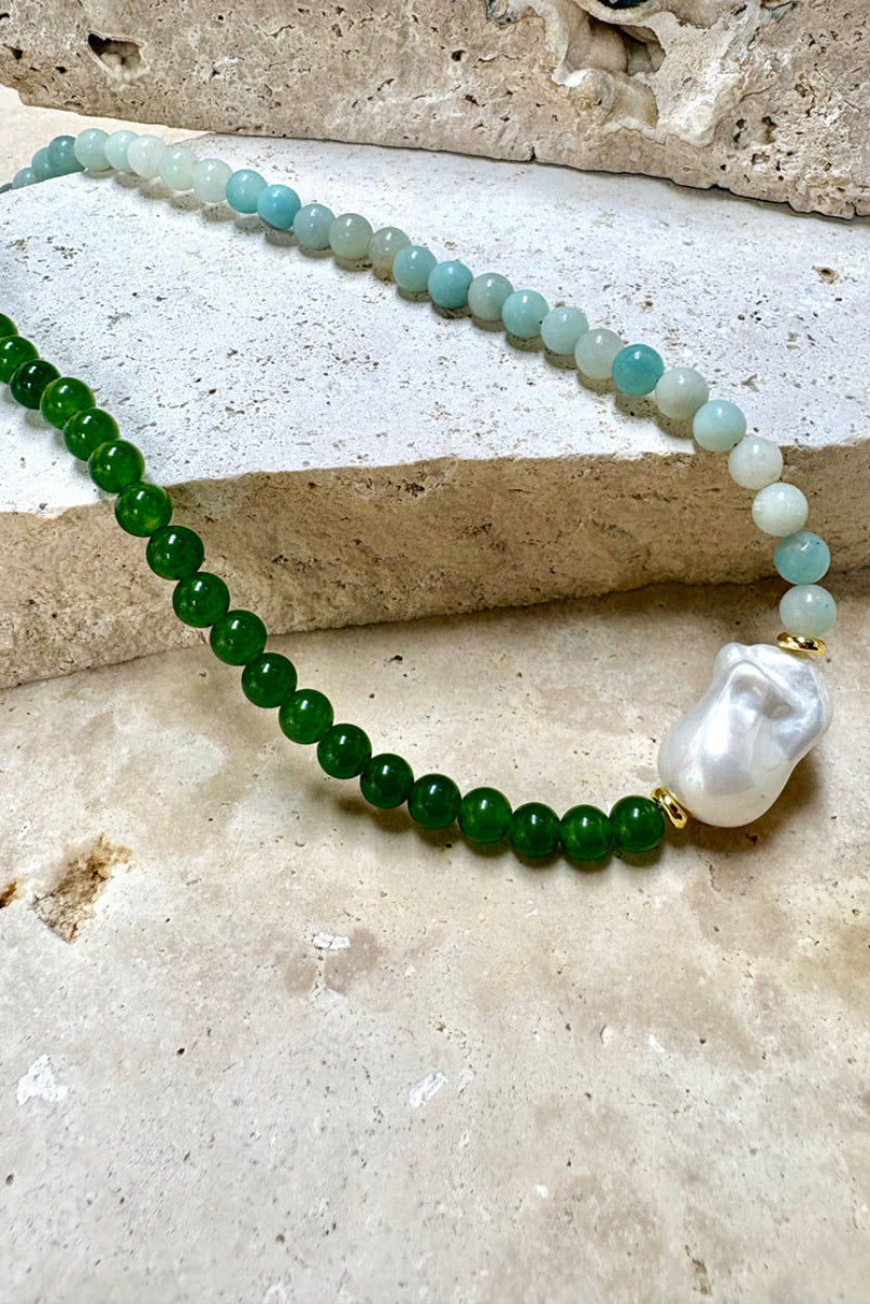 Necklace with green beads and a large white pearl pendant on a stone surface
