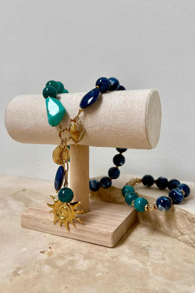 Bracelets with blue and green beads on a wooden stand against a neutral background