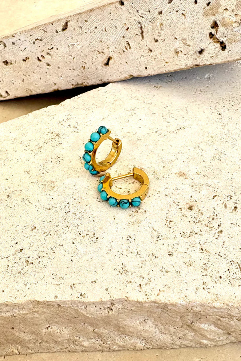 Gold hoop earrings with turquoise stones on a stone surface