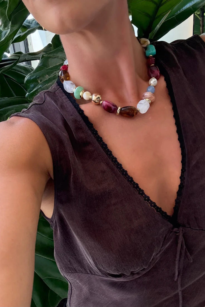 Person wearing a colorful beaded necklace with a brown top against a green leafy background