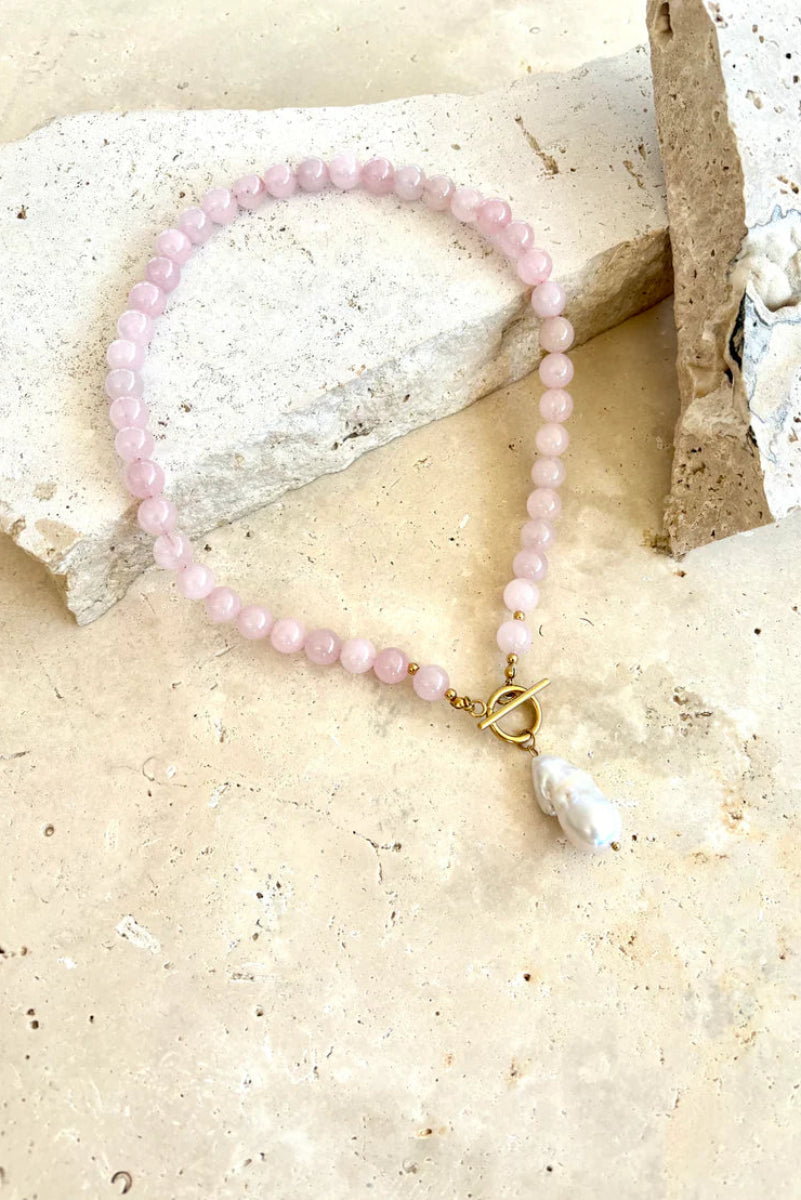 Pink beaded necklace with a gold clasp on a textured beige surface