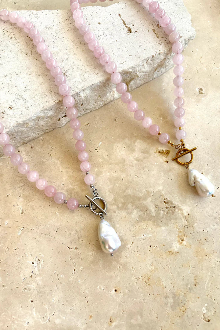 Necklace with pink beads and a pearl pendant on a stone surface