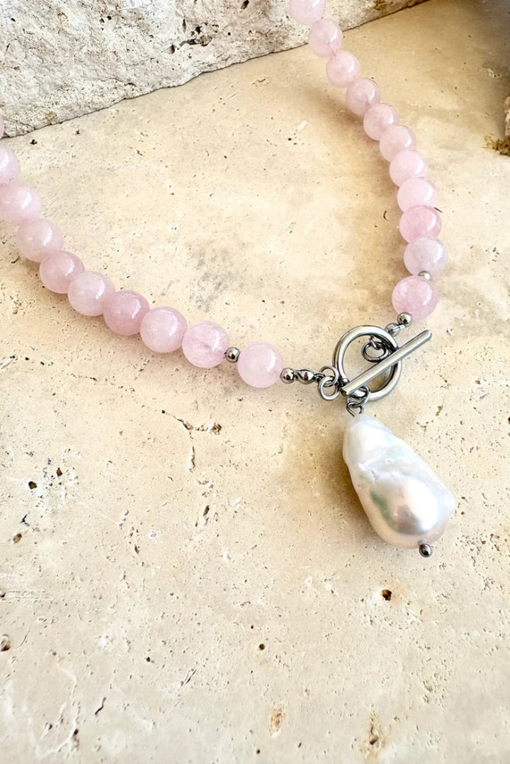 Pink beaded bracelet with a white baroque pearl on a beige stone surface
