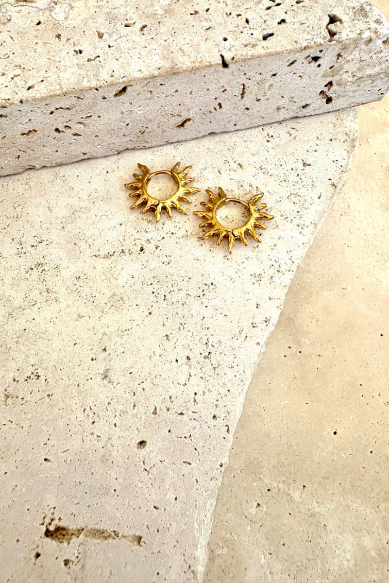 Gold sun-shaped earrings on a textured stone surface
