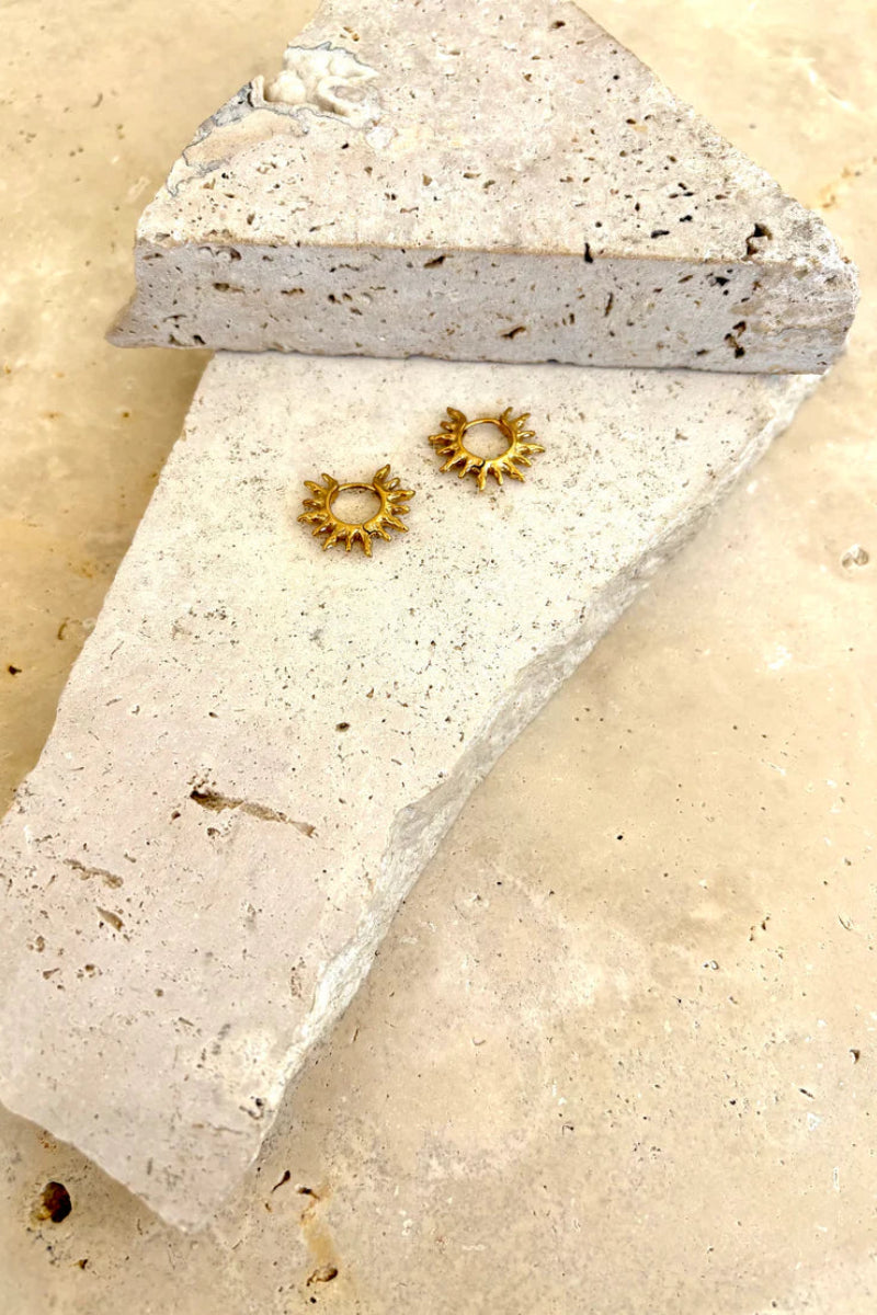 Gold hoop earrings on a textured stone surface