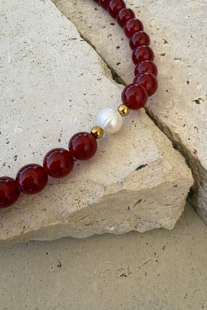 Bracelet with red beads, a gold accent, and a pearl on a stone surface