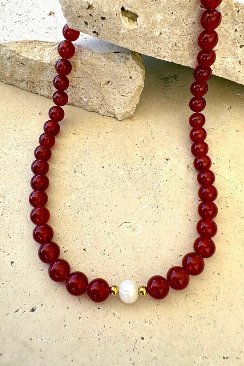 Beaded necklace with red beads and a white pearl on a stone surface