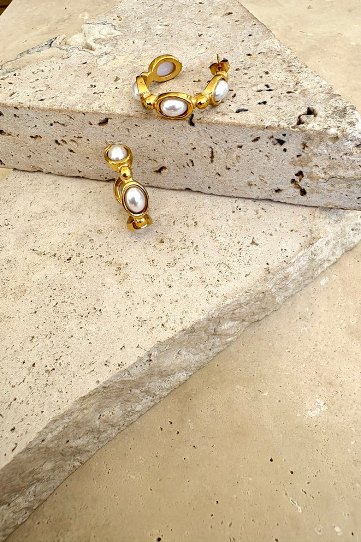 Gold and pearl earrings on a stone surface