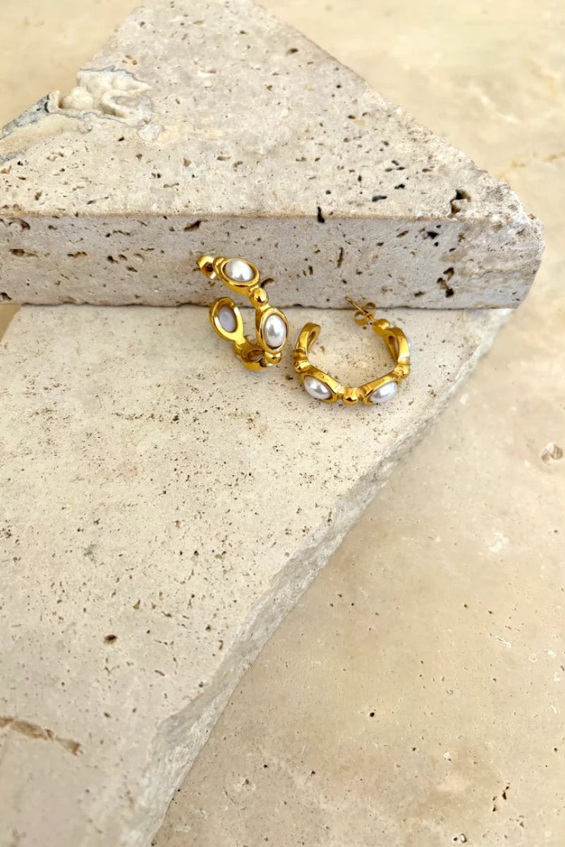 Gold hoop earrings with pearls on a stone surface