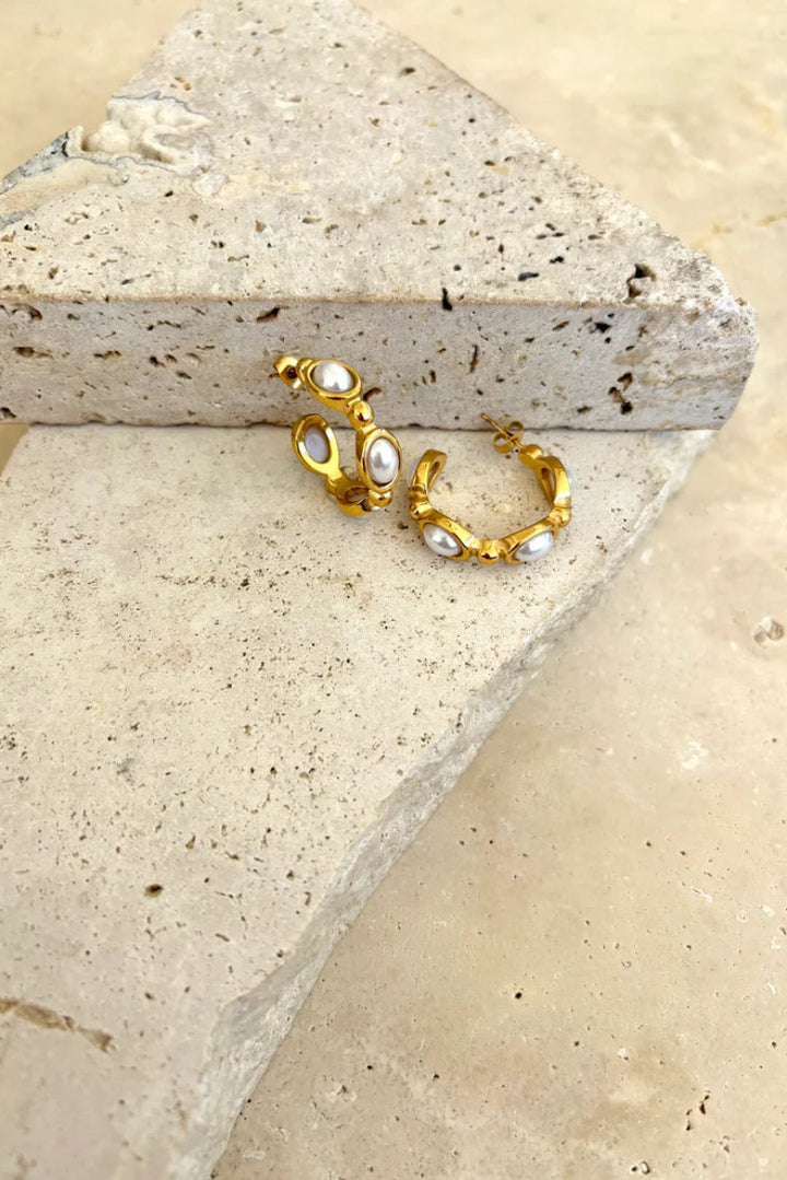Gold hoop earrings with pearls on a stone surface