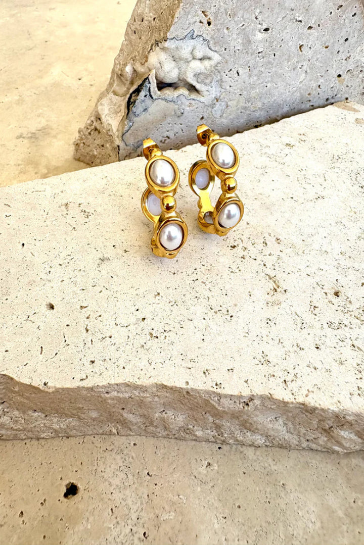 Gold and pearl earrings on a textured stone surface