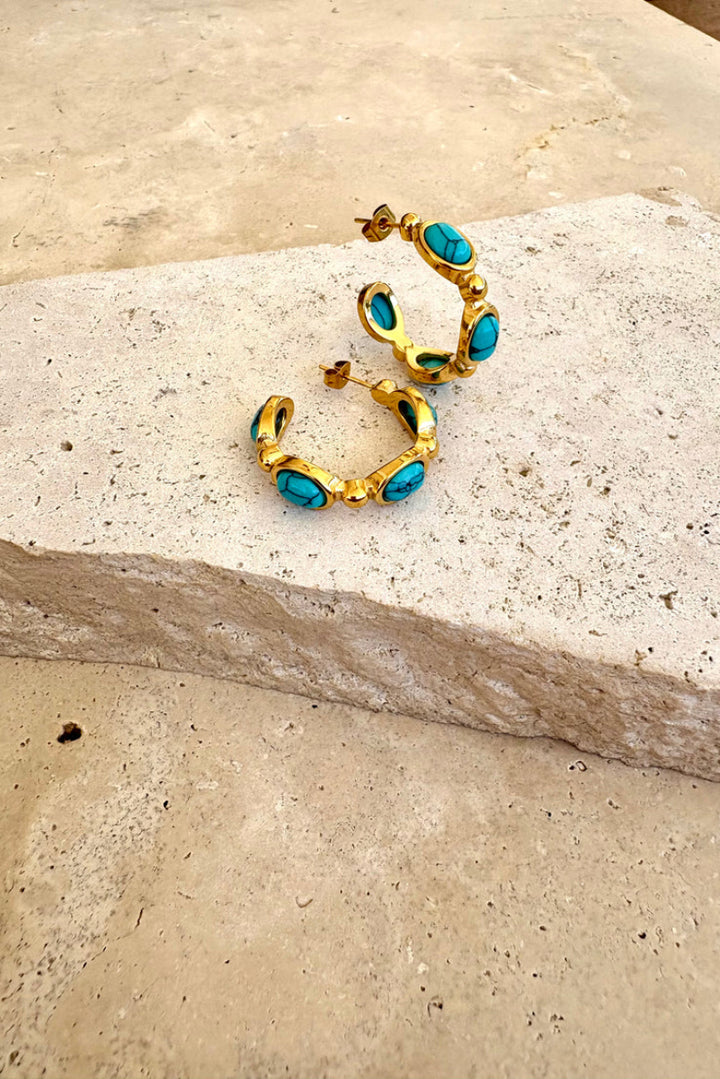 Gold hoop earrings with turquoise stones on a stone surface