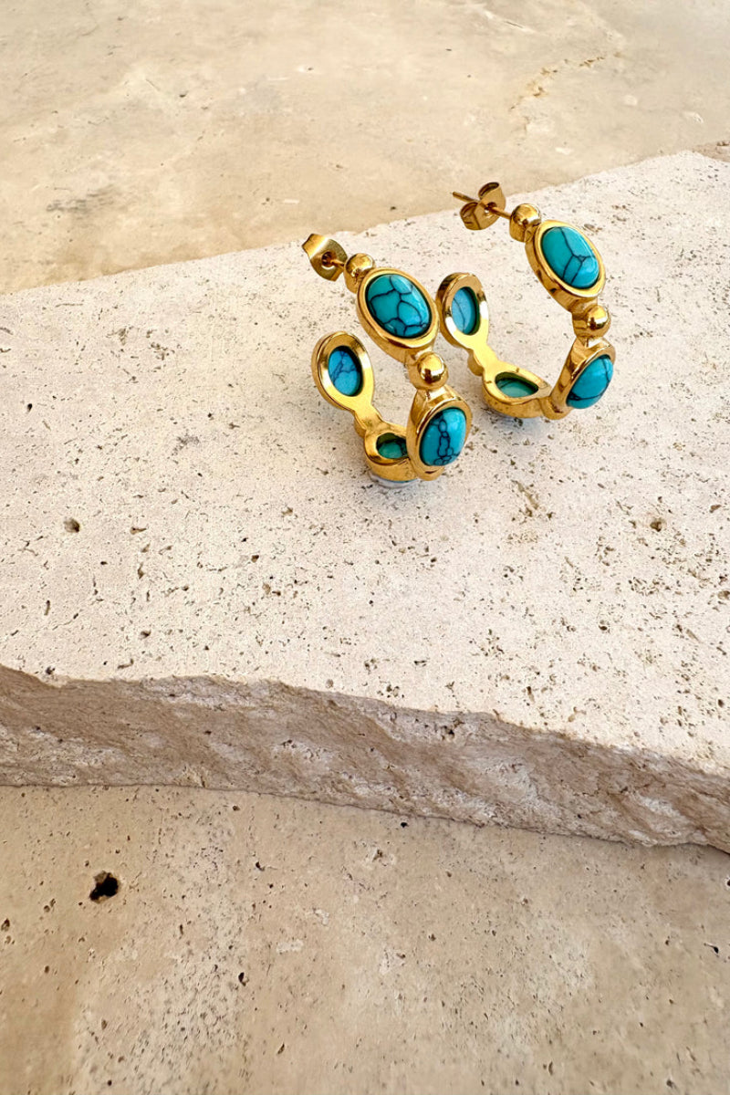 Gold hoop earrings with turquoise stones on a sandy surface