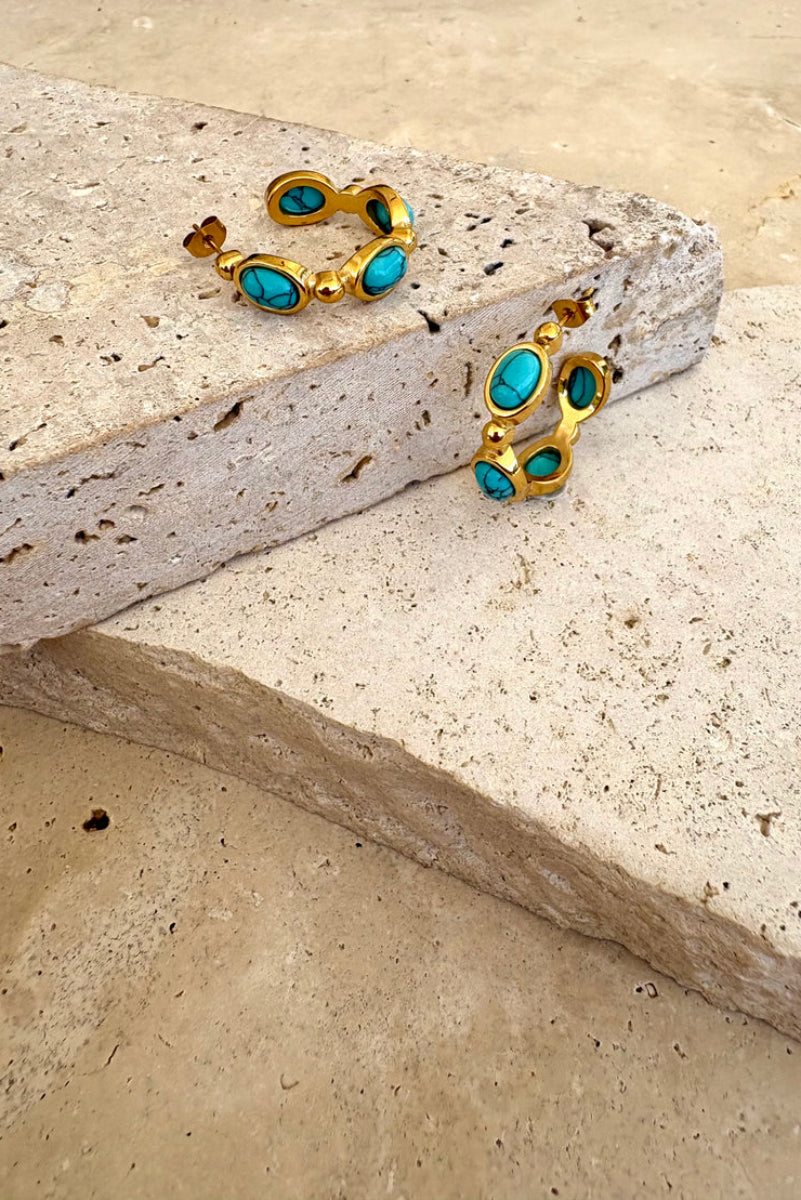 Gold hoop earrings with turquoise stones on a stone surface