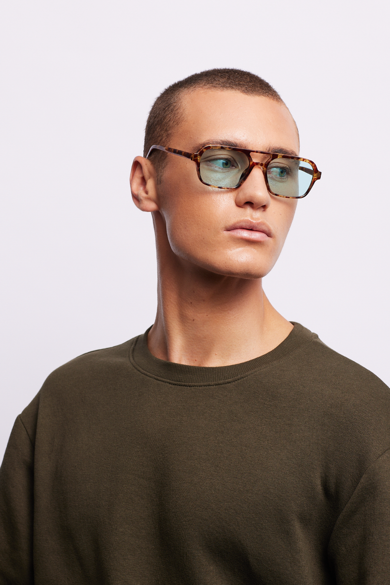 A man wearing turtle-patterned sunglasses in an aqua color.