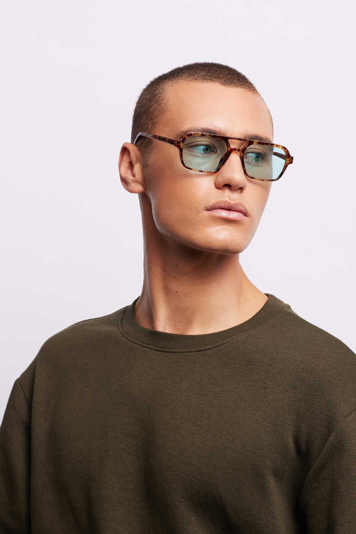 A man wearing turtle-patterned sunglasses in an aqua color.