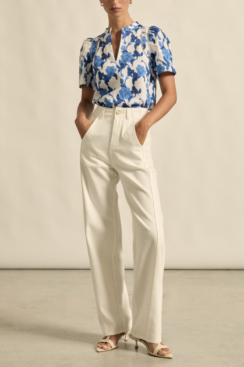 This front view of the Recollect Top in Azure Bouquet showcases its sleek silhouette, V-neckline with covered dome button, delicate lace trims, and gathered tulip sleeves.
