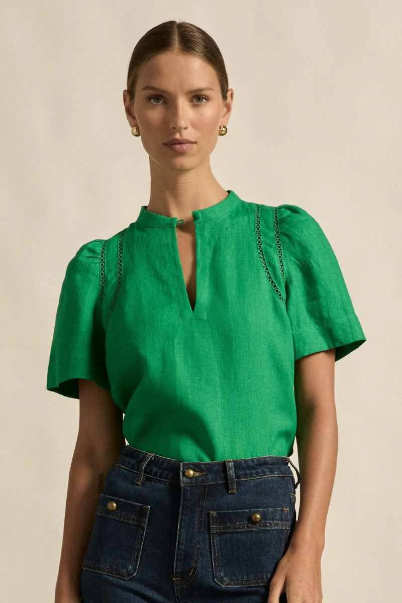Woman wearing a green blouse with short sleeves and blue jeans on a beige background